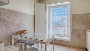 A small, modern kitchen with a glass-top table, two stools, and a view of a building with a dome through a window. - Chiado 1 - Carmo Square - Recently renovated apartment with great view of the River Taugus and São J (Lisbon)