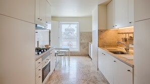 A narrow kitchen with white cabinets, a marble countertop, a sink, and a window with a view of a building. - Chiado 1 - Carmo Square - Recently renovated apartment with great view of the River Taugus and São J (Lisbon)