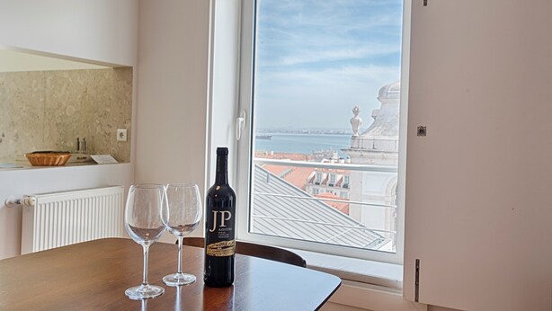A room with a view of a cityscape through a window. There is a bottle of wine and two glasses on a wooden table. - Chiado 1 - Carmo Square - Recently renovated apartment with great view of the River Taugus and São J (Lisbon)