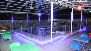 An outdoor pool area with a glass enclosure, surrounded by metal railings and tables with chairs.