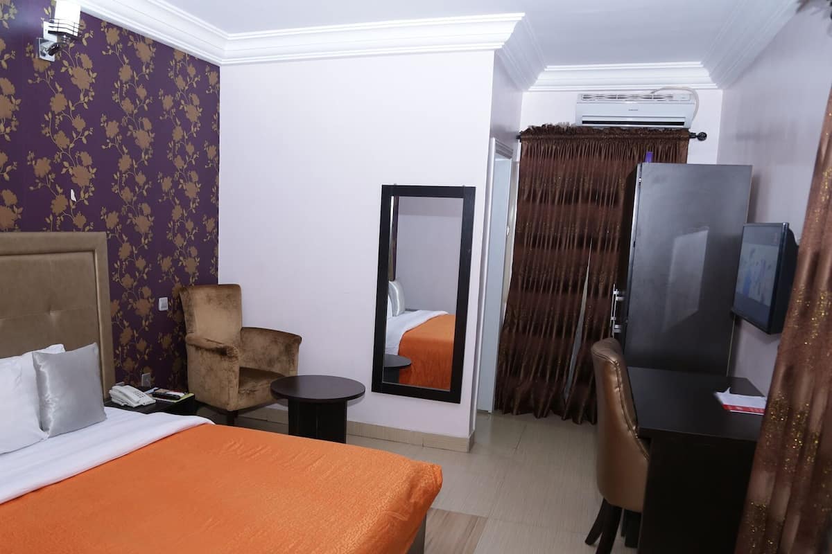 Une chambre d’hôtel comprenant un lit, une chaise, une petite table, un miroir, un téléviseur et un appareil de climatisation.