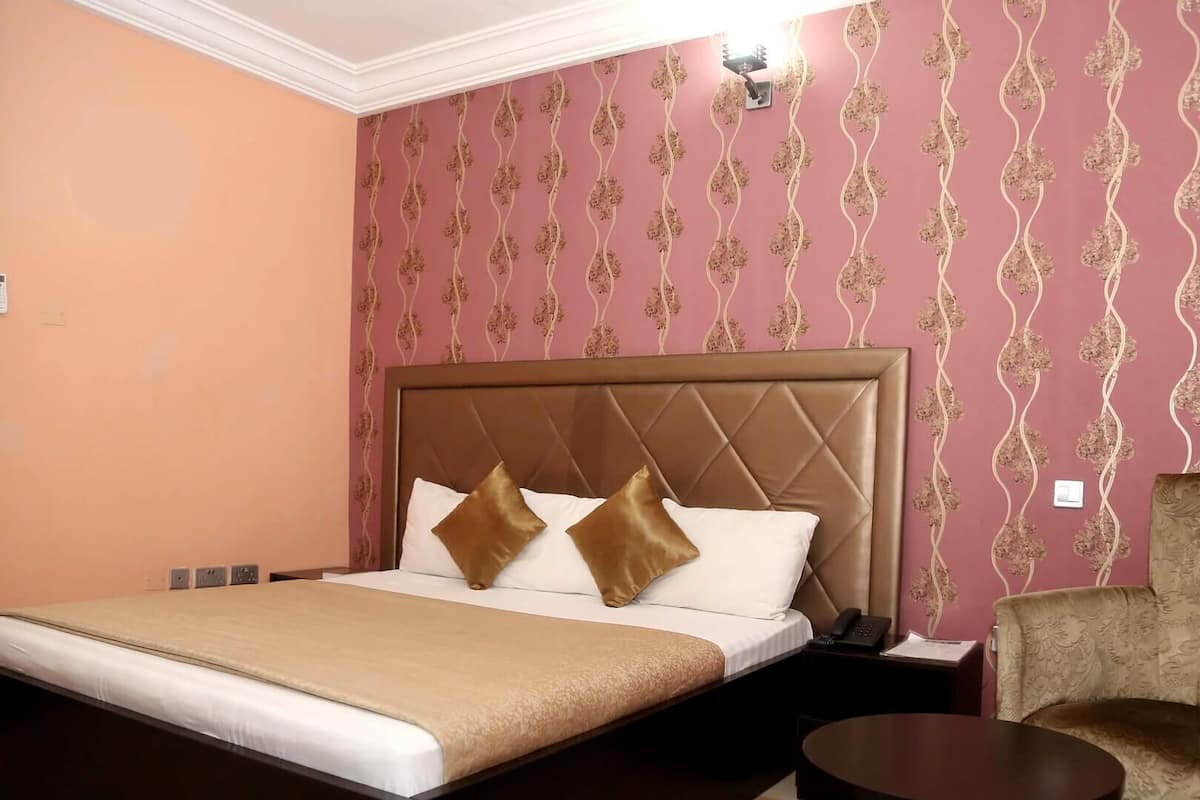 Une chambre d’hôtel avec un grand lit, une table de chevet, une chaise et un papier peint à motifs.