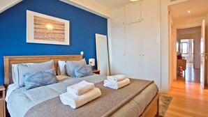 A bedroom with a large bed, a wooden headboard, a blue accent wall, a framed picture, and a wardrobe.