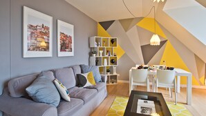 A modern living room with a grey sofa, a dining table with chairs, and a geometric wall design.