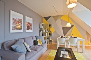 Een moderne woonkamer met een grijze bank, een eettafel met stoelen en een geometrisch wandontwerp.