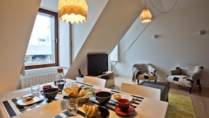 A modern dining area with a table set for breakfast, a television, and two upholstered chairs.