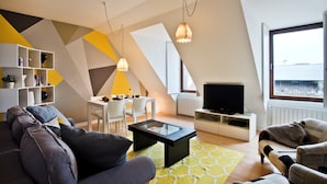 A modern living room with a sofa, coffee table, and TV, a dining area with chairs, and a large window with a view.