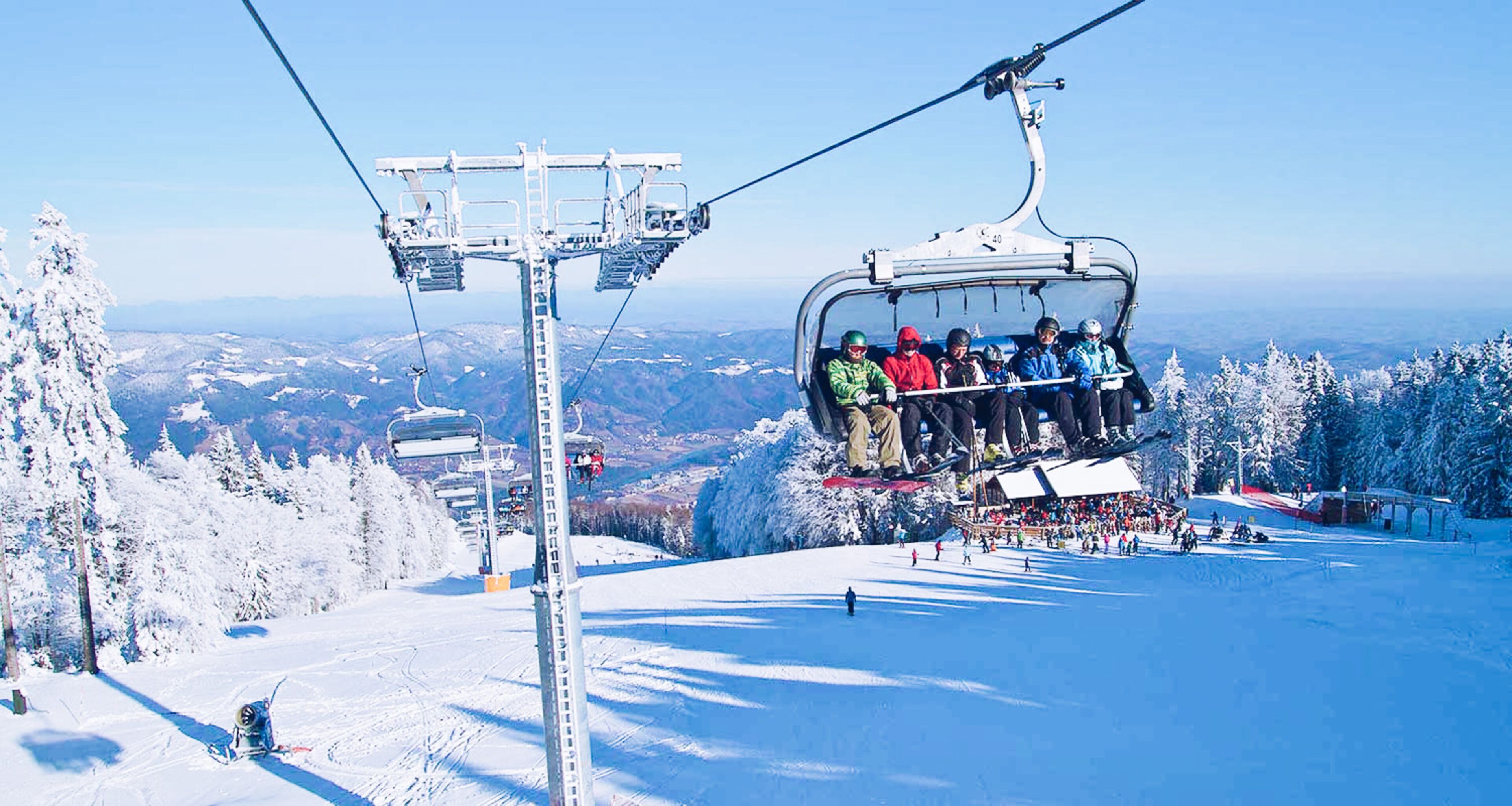 A ski lift with passengers, surrounded by snow-covered trees and a clear sky.
