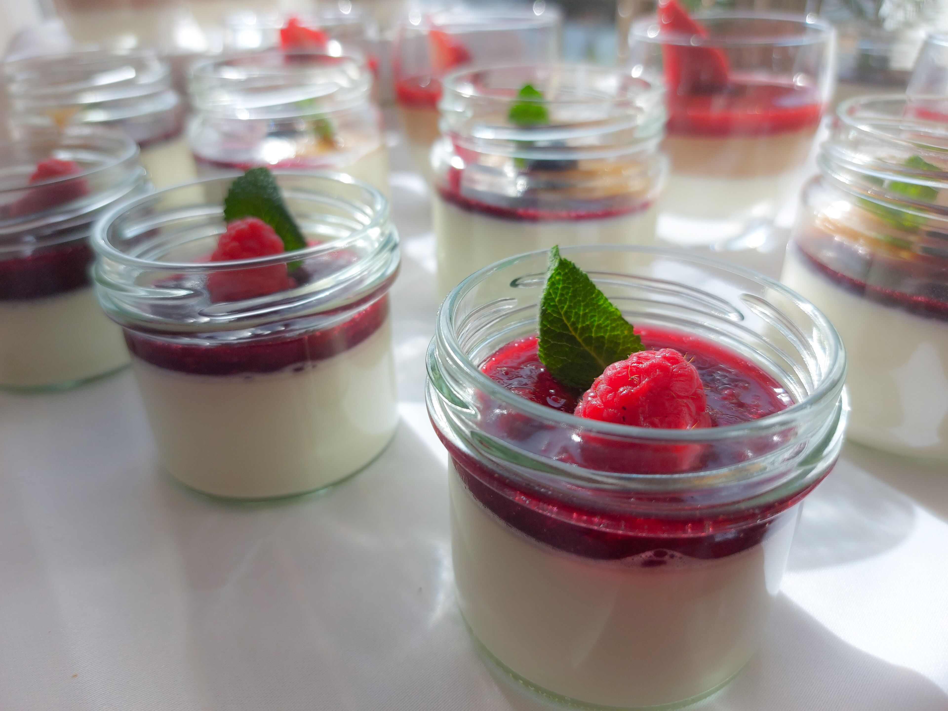 Une série de bocaux en verre contenant des desserts en couches, à base de framboises et de feuilles de menthe.