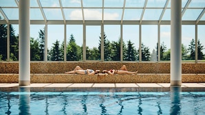 A swimming pool with a tiled edge, a mosaic-tiled bench, and a view of trees through large windows. - Pohorje Village Wellbeing Resort – Wellness & Spa Hotel Bolfenk (Maribor)