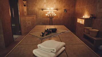 Un cuarto de spa con piso de baldosas, una camilla de masaje, una planta pequeña y un estante con velas.
