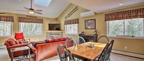Amplia sala de estar con chimenea, comedor con mesa y sillas de madera, y ventanas grandes con cortinas a cuadros.