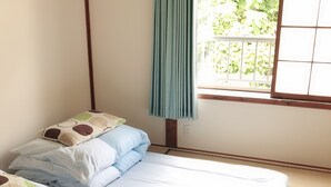 A room with two beds, a window with a curtain, and a view of greenery outside.