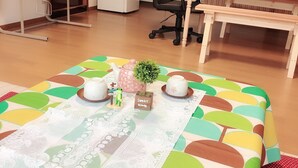 A cozy room with a wooden floor, a dining table with chairs, a small kitchen area, and a bed with a colorful bedspread.
