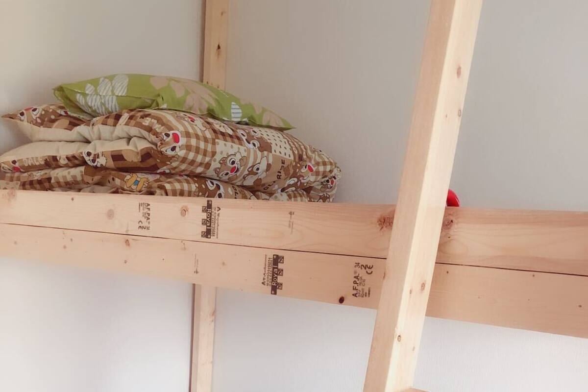 A bunk bed with a lower bunk covered in a light blue blanket and a pillow, and an upper bunk with a patterned blanket and pillows.