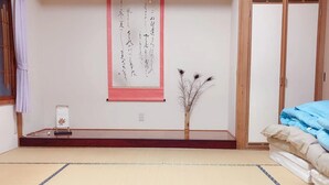 A traditional Japanese room with tatami flooring, a shoji screen, a small bonsai tree, and a bed with blue bedding.