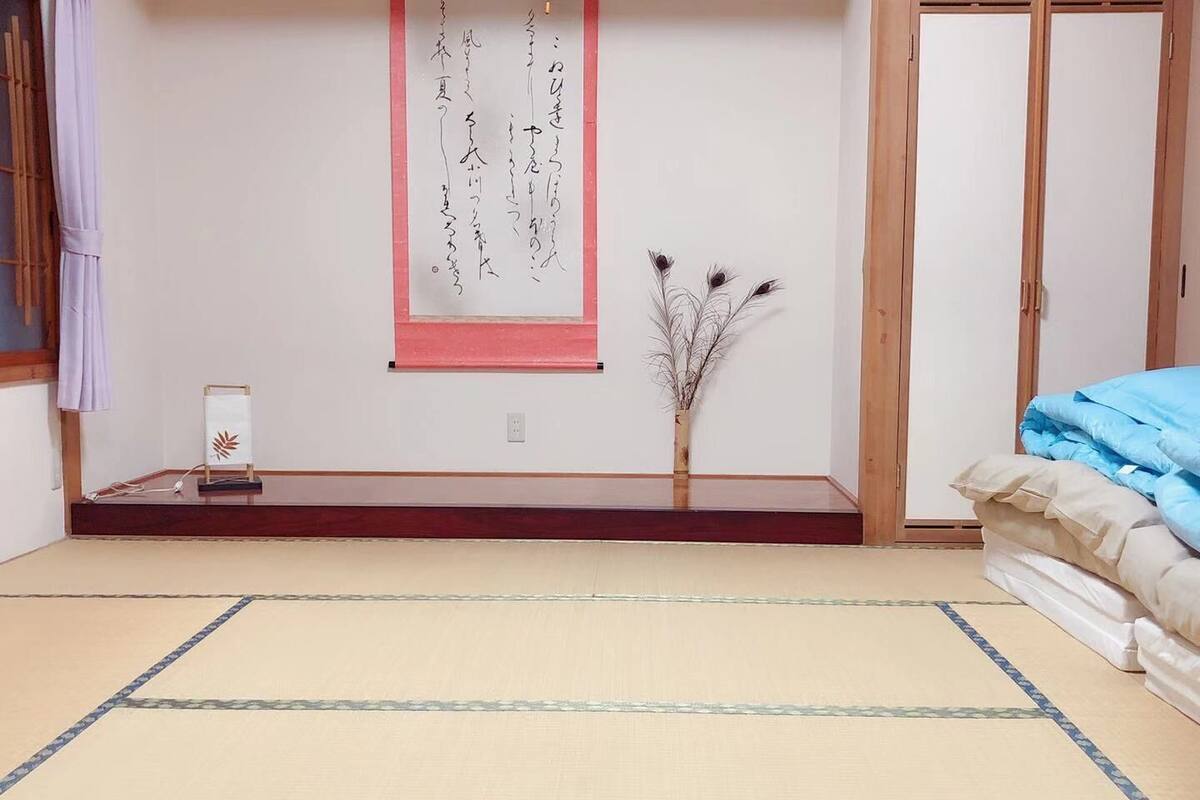 A traditional Japanese room with tatami flooring, a shoji screen, a small bonsai tree, and a bed with blue bedding.
