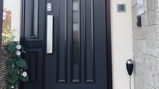 A black door with a handle and a peephole, a wall-mounted intercom, and a small sign with a number.