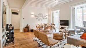 A spacious living room with a wooden floor, a dining area with a round table and chairs, a sofa, and a television.