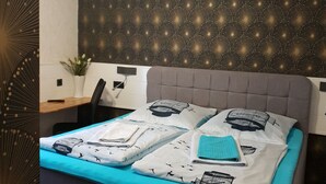 A neatly made bed with a blue bedspread and white pillows, a grey headboard, and a wall with a starry pattern. - Waldhotel und Restaurants Lemberg (Hagen)