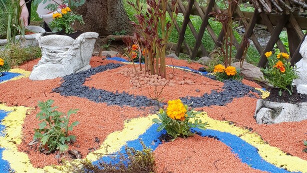 A garden with a colorful pebble path, a large tree, and a statue. - Waldhotel und Restaurants Lemberg (Hagen)
