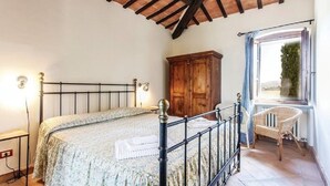 Une chambre à coucher avec un lit, une armoire en bois et un fauteuil en osier.