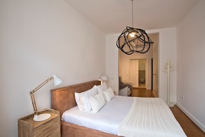 A bedroom with a wooden headboard, a white bedspread, two bedside lamps, and a hanging light fixture.