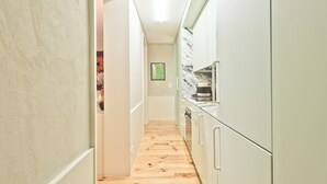 A narrow hallway with wooden flooring, white walls, and a kitchen area with cabinets and appliances.