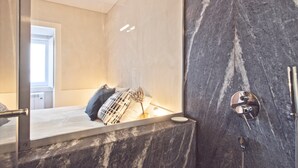 A modern bathroom with a marble wall, a glass shower enclosure, and a visible towel rack.