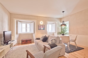 A modern living room with a sofa, armchairs, a television, and a dining area with a table and chairs.