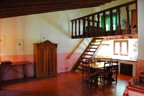Uma sala de jantar com mesa e cadeiras de madeira, uma escada que leva a um andar superior e um armário de madeira.