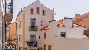 Une rue étroite bordée de voitures garées et d’un café appelé « CAFETERIA NANDO » qui dispose de tables en terrasse.