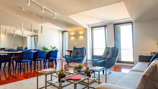 A spacious living area with a dining table, blue chairs, a sofa, and a coffee table.
