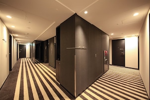 Pasillo de hotel con alfombra a rayas, paredes oscuras y puertas numeradas del 410 al 415.
