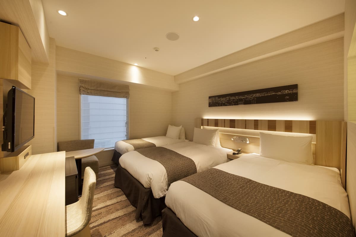 A hotel room with three beds, a desk, and a television.