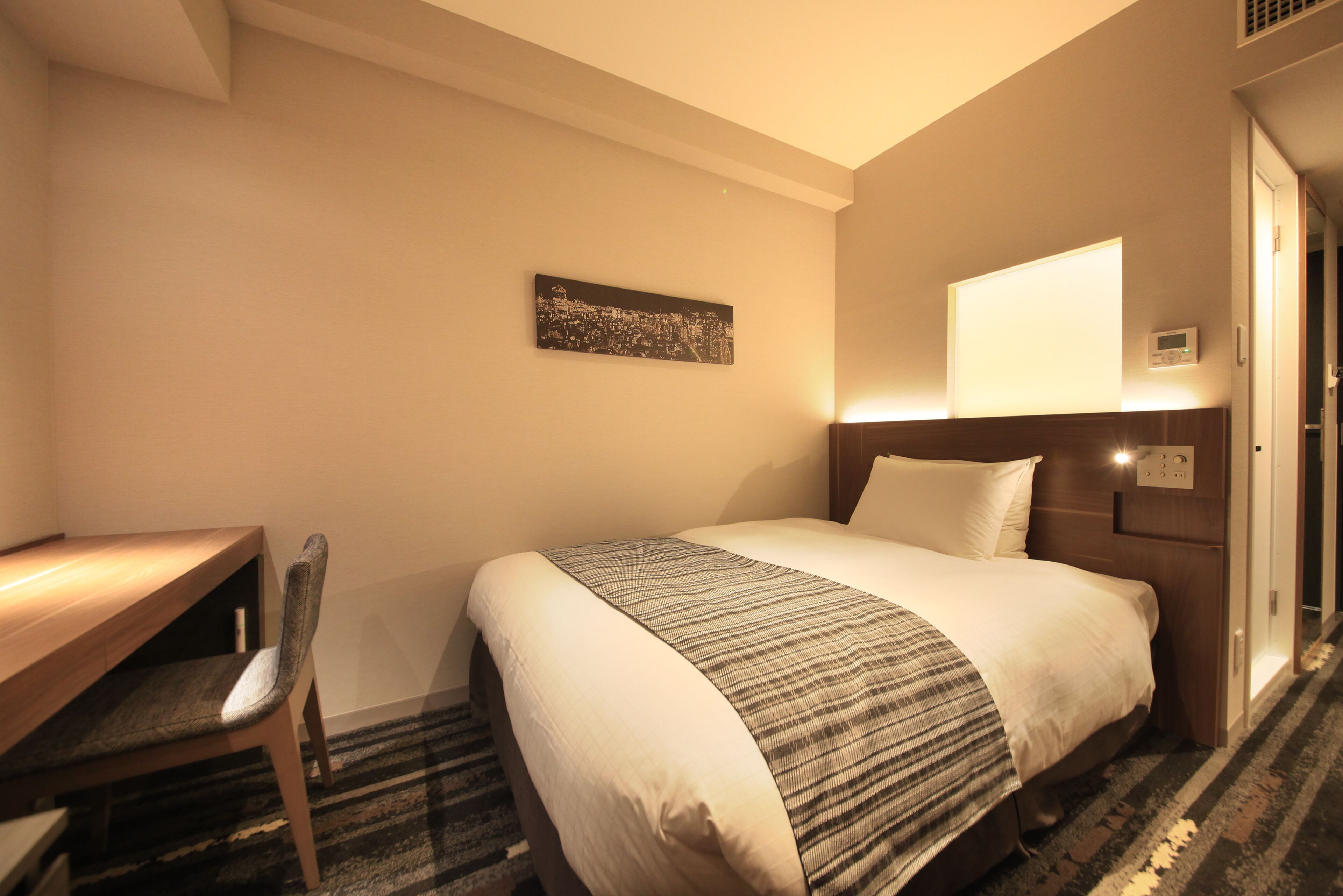 Una camera d'albergo con un letto, una scrivania, una sedia, una TV a parete e un quadro.
