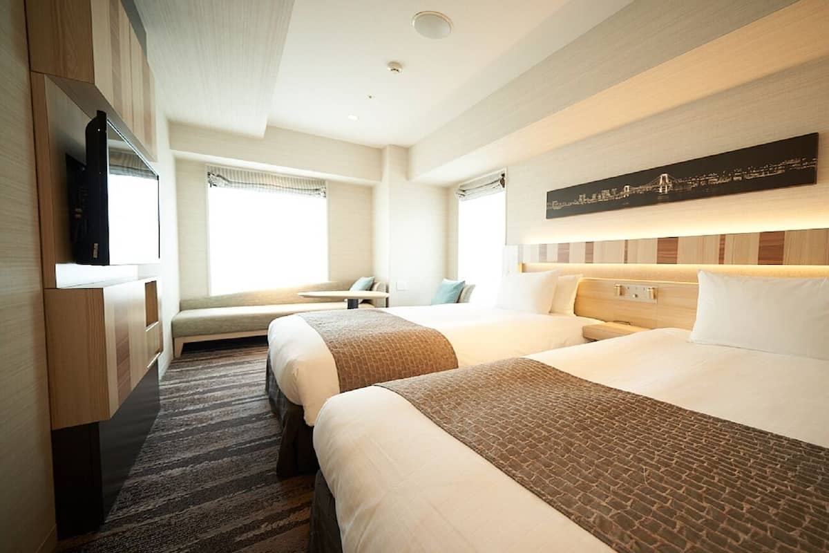 A hotel room with two beds, a desk, a chair, and a television.