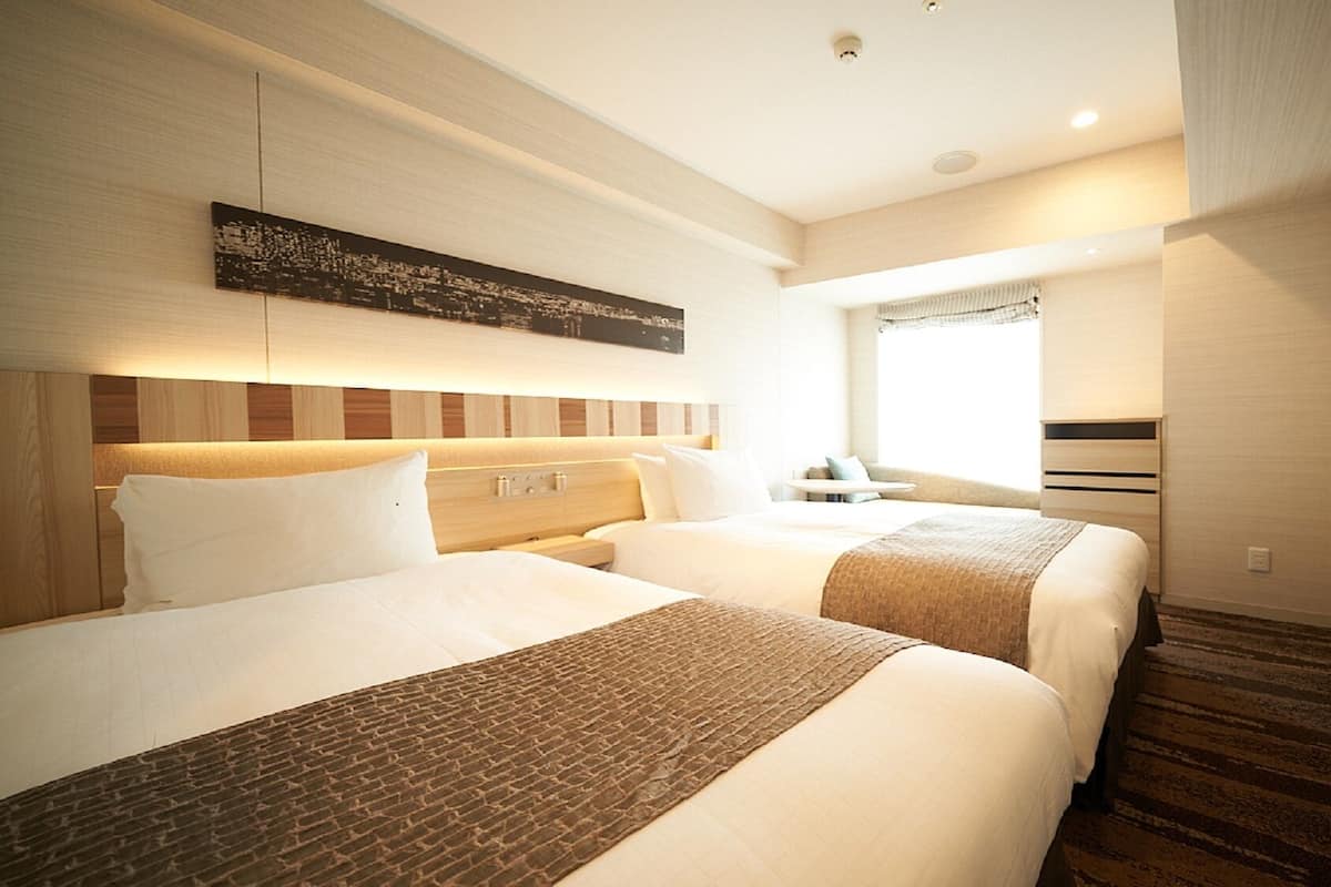 A hotel room with two beds, a flat-screen TV, a window with curtains, and a wall-mounted artwork.