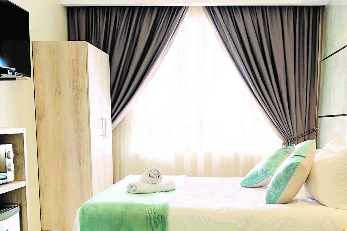 Une chambre d’hôtel avec un lit, une armoire et une fenêtre avec des rideaux.