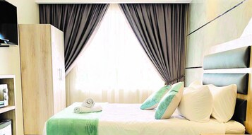 Habitación de hotel con cama, armario y ventana con cortinas.