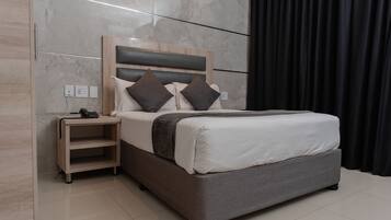 Quarto de hotel moderno com uma cama grande, uma mesinha de cabeceira e um criado-mudo.