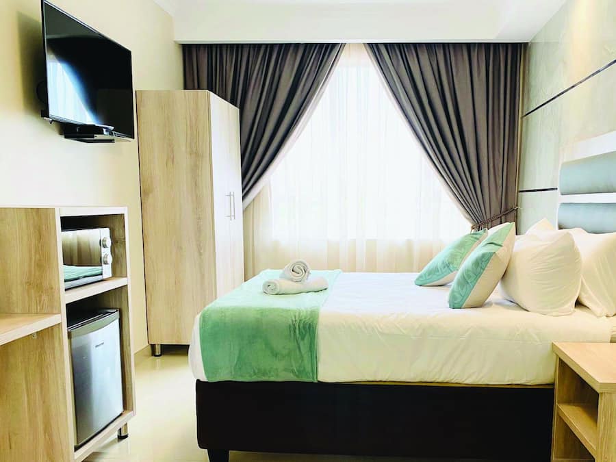 Ein Hotelzimmer mit einem Bett, einem an der Wand befestigten Fernseher, einem Kleiderschrank und einem kleinen Tisch.