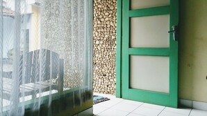 Een kamer met een groene deur, een raam met dunne gordijnen en een betegelde vloer.