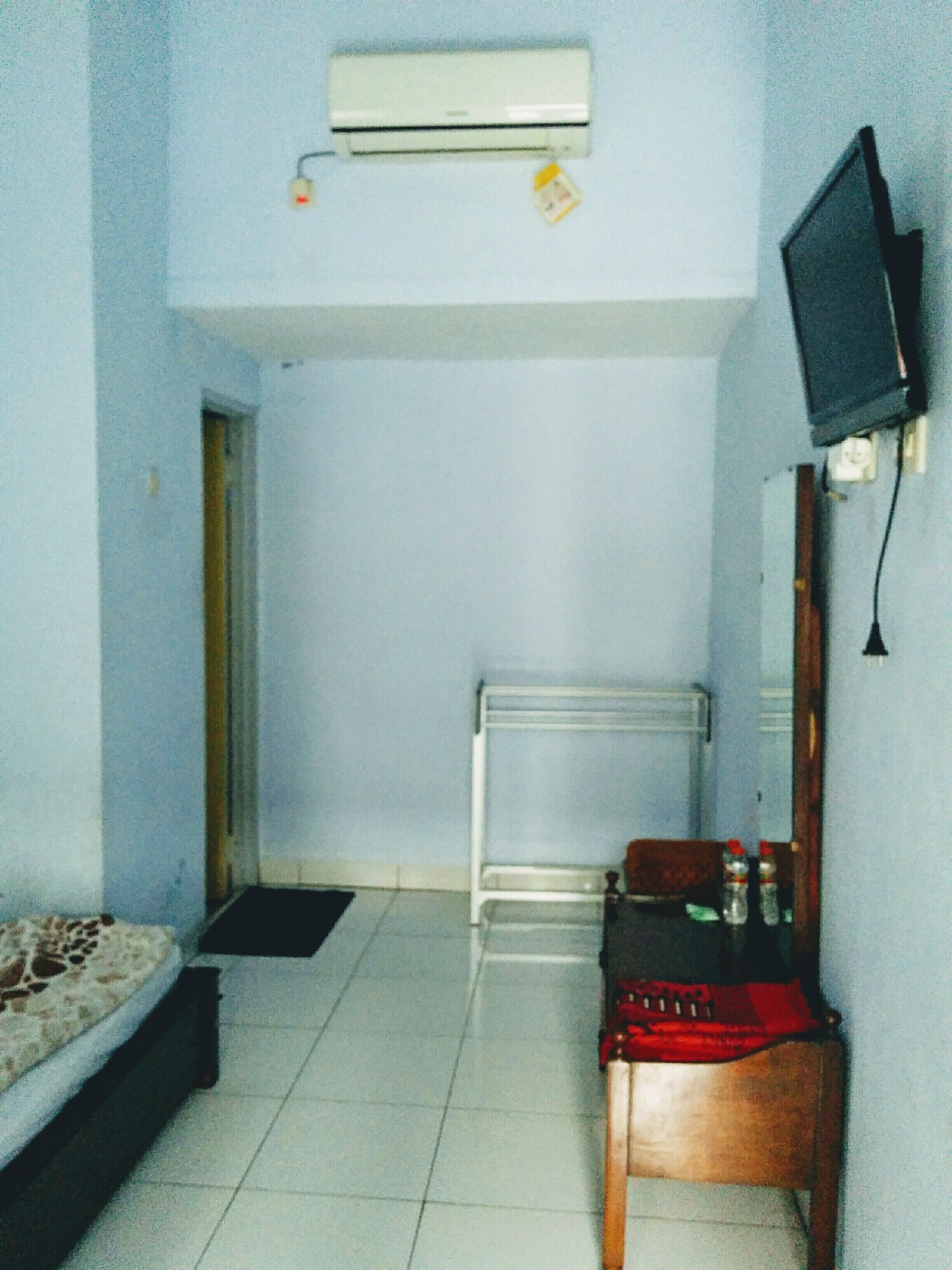 A small, sparsely furnished room with a bed, a desk, a chair, a radiator, and a television mounted on the wall.