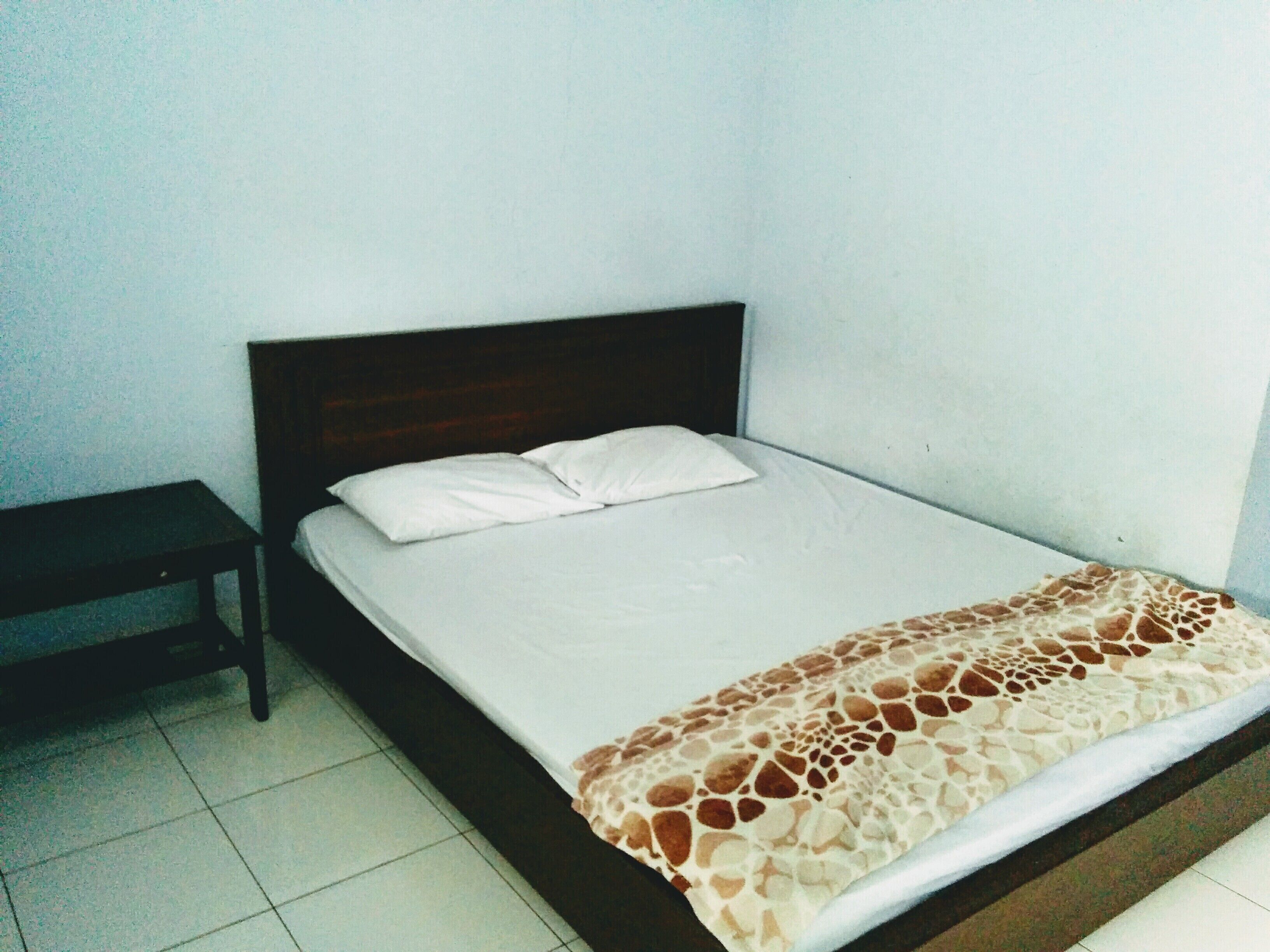 Un lit simple avec une tête de lit en bois, un matelas blanc et une couvre-lit à motifs.
