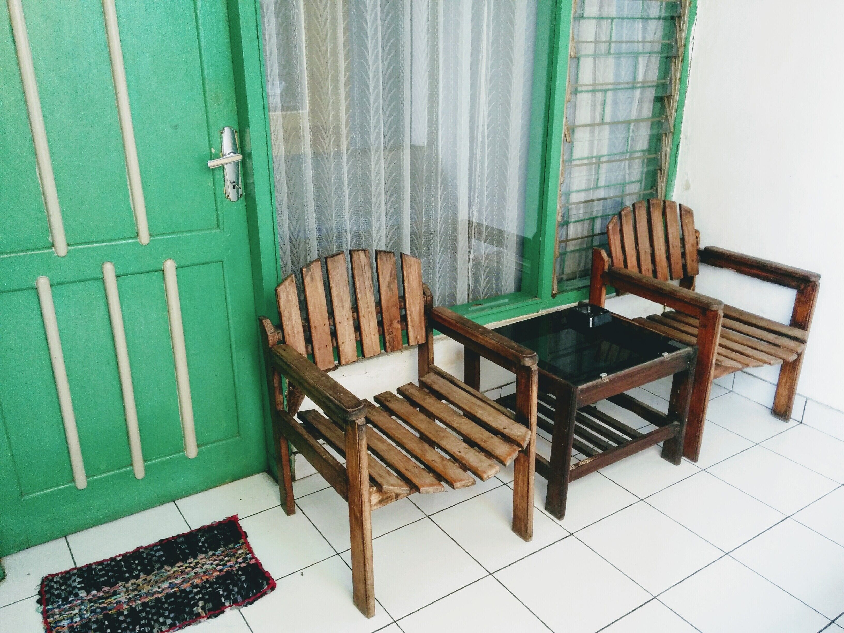 Een kamer met een groene deur, twee houten stoelen en een glazen tafel, en een kamerbreed tapijt op de vloer.