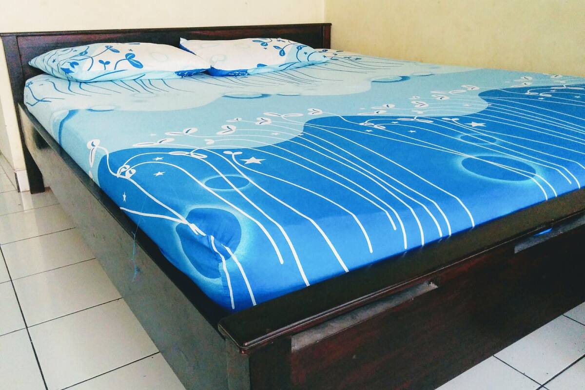 Un lit avec une couvre-lit à motifs bleus et blancs, une tête de lit en bois et un sol carrelé.