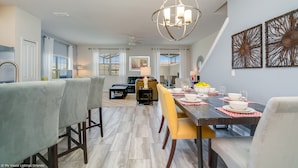 A dining area with a wooden table set for four, a chandelier, and a view of the living room in the background. - Stunning Lakeview Townhome w/ Private Pool! (Kissimmee)