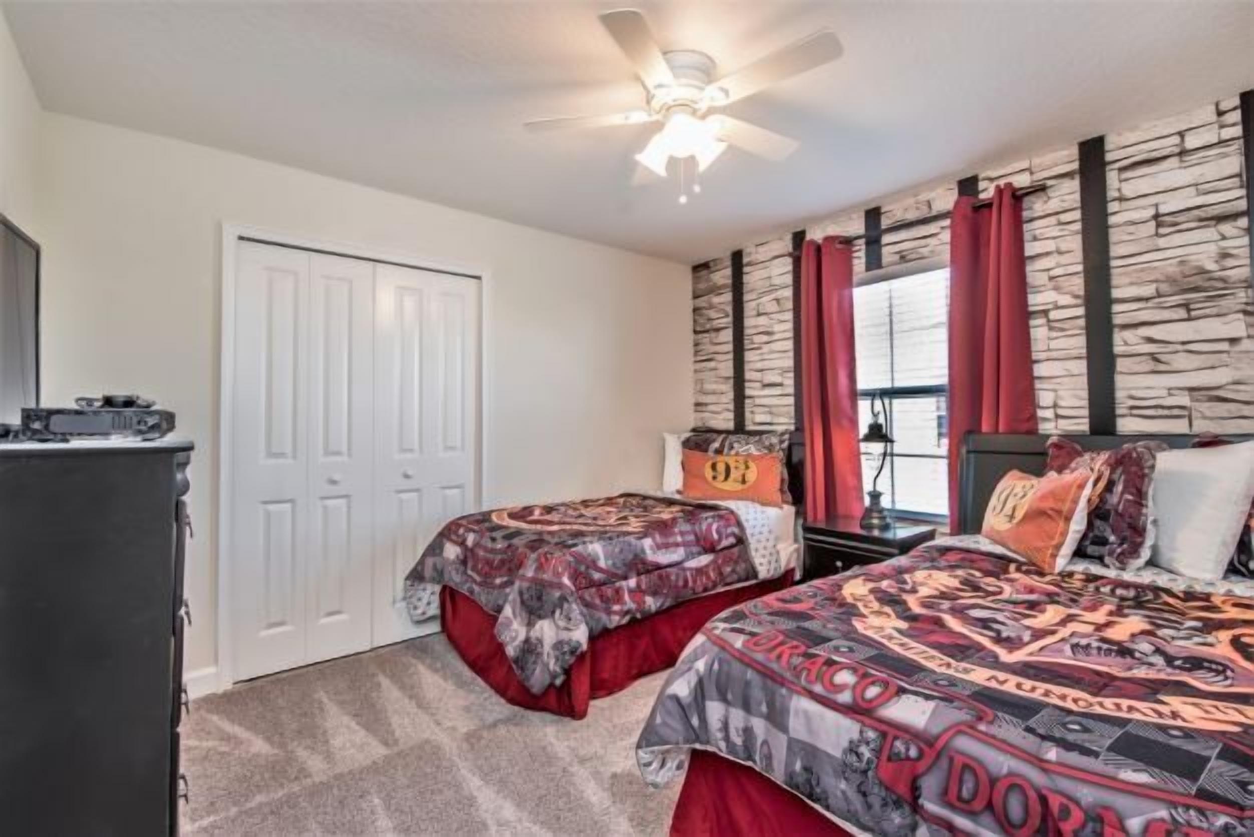 A bedroom with two beds, a ceiling fan, a wardrobe, and a stone-patterned wall.