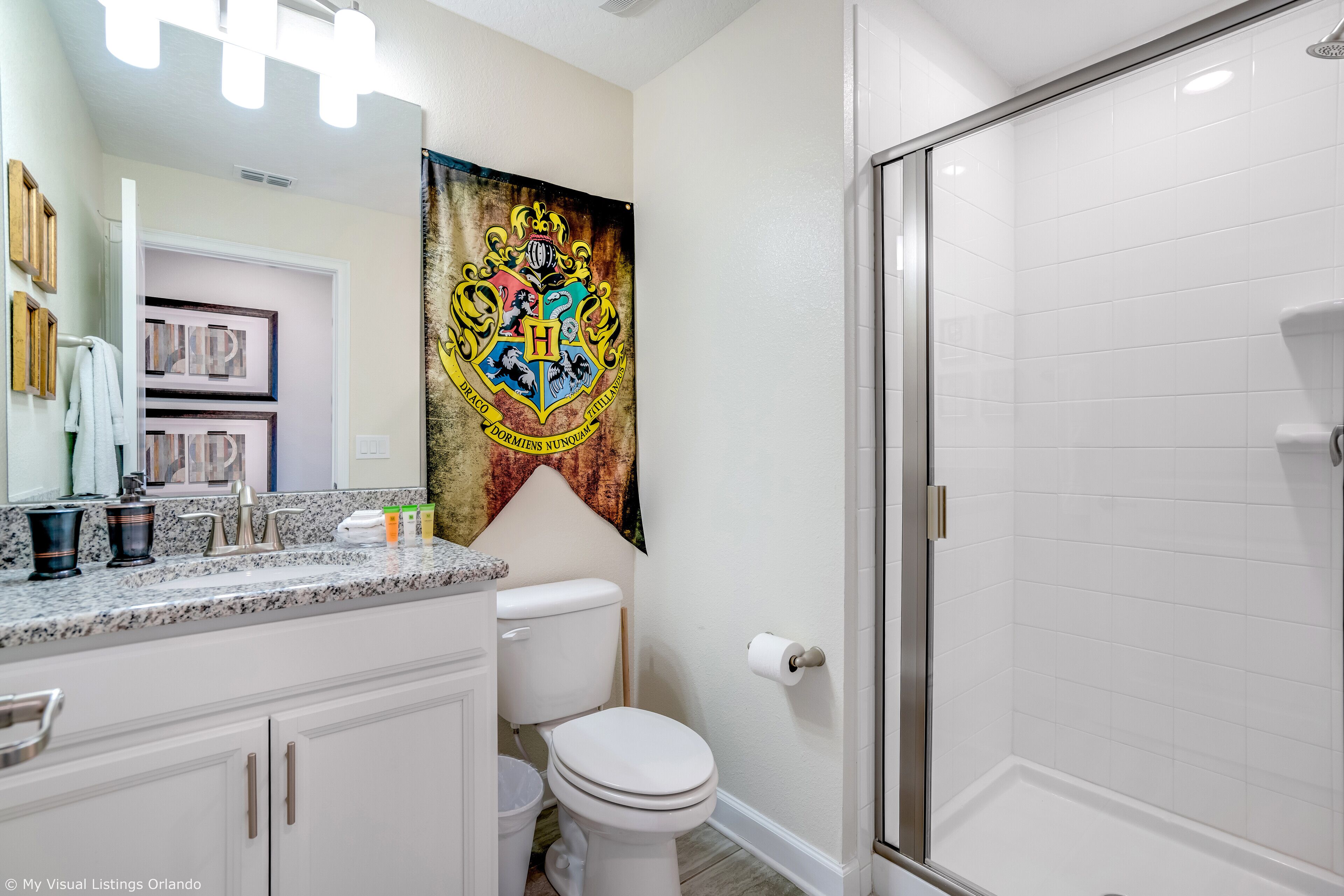 Une salle de bain avec des toilettes blanches, une douche, un meuble-lavabo avec un miroir et un porte-serviettes.